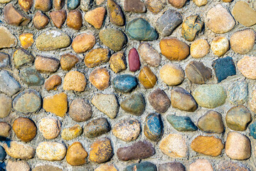 multi-colored and multi-textured pebble stones lie in rows partially pressed into the main covering of a horizontal or vertical surface