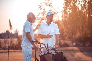 Two older men stand on a golf course and talk. Talk about golf.