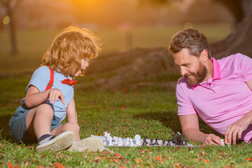 Fototapeta premium Father and son playing chess spending time together in park. Active people having fun and playing chess at park, spend time with child.