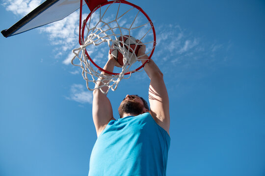 Basketball player making a jump shot against blue sky background.