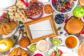 Various traditional breakfast food - fried eggs with bacon, muesli, oats, waffles, pancakes, burger, croissants, fruit berry, coffee, tea and orange juice, white table background copy space top view
