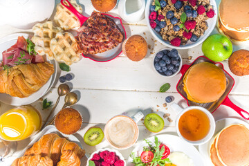 Various traditional breakfast food - fried eggs with bacon, muesli, oats, waffles, pancakes, burger, croissants, fruit berry, coffee, tea and orange juice, white table background copy space top view