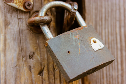 Old Lock Hanging On A Wooden Wall Or Brown Door Close-up. A Rusty Vintage Style Barn Copper Lock. A Metal Antique Device For Closing Doors. Protection Against Burglars And Thieves. High Quality Photo.