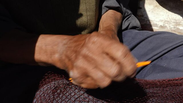 An old fisherman mends a commercial fishing net with needle and thread at the harbor in Essaouira, Morocco. Handicraft.