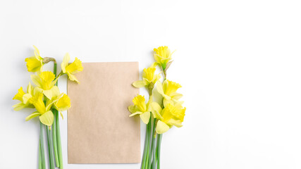 holiday banner. composition of spring yellow daffodils flowers and craft paper notebook on white background. simple flat lay, space for text. flat lay