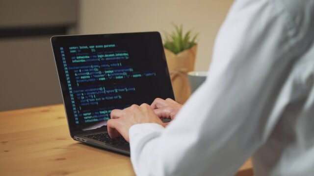 Male programmer is working on creating software, typing program code on a laptop keyboard, programmer at work, a freelancer at remote work at home.