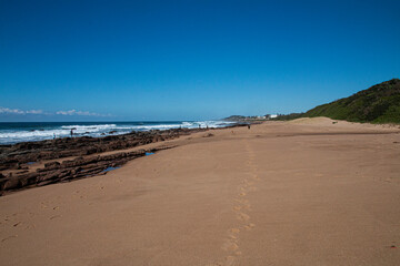 Fototapeta na wymiar Stretch of Beach and Vegetation with Layered Rocks on Shoreline