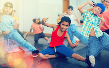 Multiethnic group of children in casual wear training hip hop movements in dance class with female...