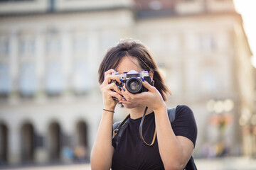  Young woman taking photo in the city with camera. I should definitely get a picture of that. - obrazy, fototapety, plakaty