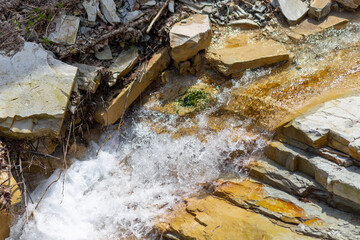 mountain blue water flows down from gray stones waterfall in summer close-up