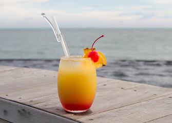 Glass of fruit mocktail with red cherry by the beach with ocean view