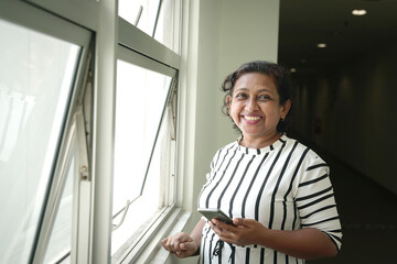 Fototapeta premium Portrait of Asian Indian ethnicity businesswoman holding cellphone and smiling at the camera.