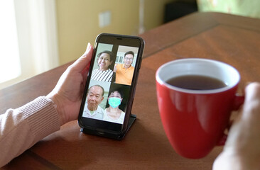 Woman having group video call with colleagues over smartphone, while drinking her coffee.