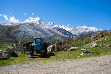 old blue tractor in the village on the background of snowy mountains