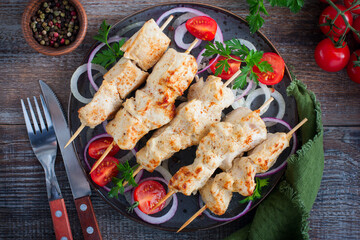 Chicken breast kebab, baked in the oven on wooden skewers on a plate, horizontal, top view