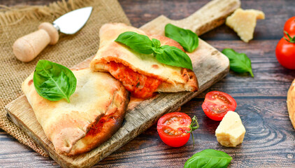 Fototapeta na wymiar Home made italian calzone vegetarian pizza with tomatoes, mozzarella and parmesan cheese and fresh basil 