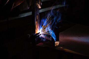 A man welder with construction gloves and a welding mask is welded with a welding machine metal in...