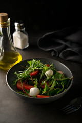 light snack. fresh green salad with lettuce leaves and arugula greens. with cherry tomatoes and mozzarella cheese. low key, dark mood, copy space. for menus and magazines with recipes