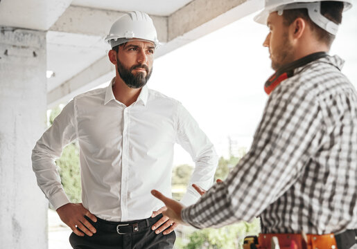 Male contractors in hardhats talking about project at construction site