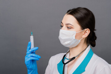 Serious female doctor in medical mask holding syringe isolated on grey