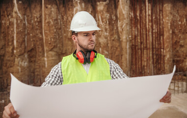 Serious builder with blueprint at construction site
