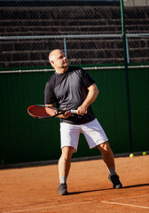 An adult man plays tennis on a street court on a sunny day. Sports and active lifestyle. Vertical.