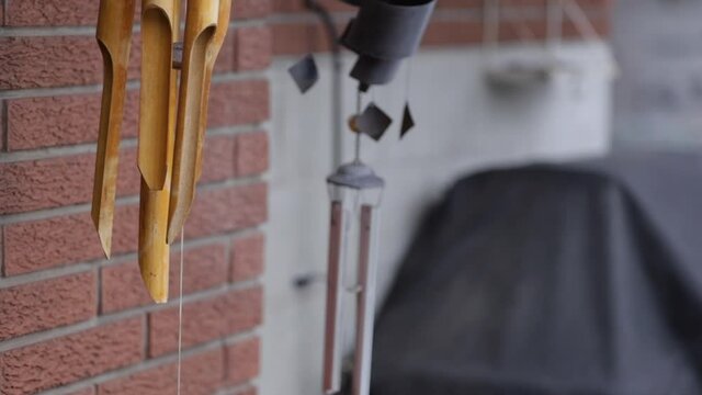 Tilt Up Shot Of Wind Chimes Blowing In The Wind With Rustic Brick Wall In The Background, Windy Overcast Day. 