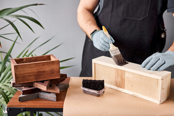Man carpenter varnishing wooden crate with brush in her small business. In your work, do you use stains or wood preservatives to show the wood pattern.