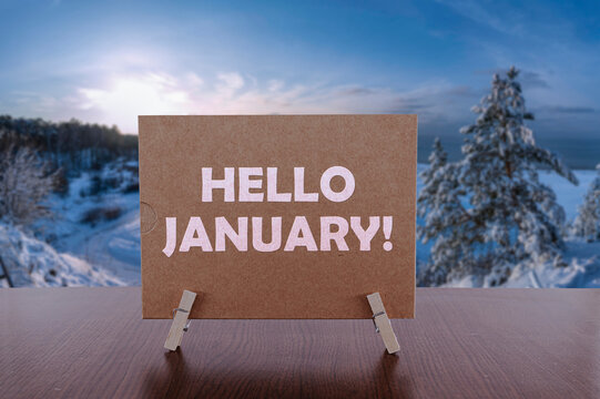 Hello January text on card on the table with sunny winter landscape background.