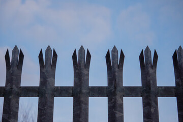 Metal anti climbing fence with spikes on top against blue sky. Safety and protection concept