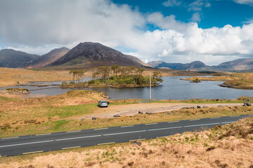 Twelve pines island in Connemara, small car and road, county Galway, Ireland, popular tourist destination. Mountains in the background. Beautiful cloudy sky. Irish landscape