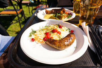 Sausage with salad on a plate and light beer on a tray. Street food and beer festival on a sunny day. Food for a friendly campaign and a picnic in nature