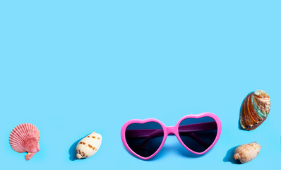 Pink heart shaped sunglasses with exotic sea shells on blue background. Summer background concept