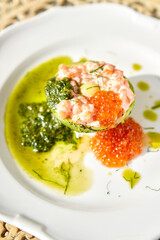 Raw salmon tartare. Fresh salmon, avocado and pesto sauce with red caviar on a plate. Selective focus