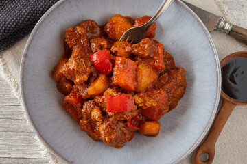 A bowl of fresh cooked filipino pork stew isolated on wooden table from above