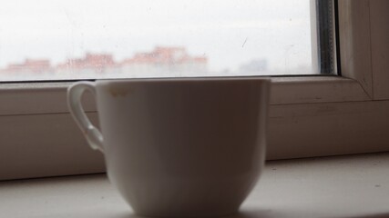 Close up white coffee cup with on the windowsill. pours coffee near window with light shade 