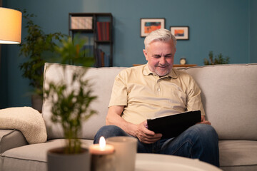 Fototapeta premium Smiling grey-haired man relaxing in living room with tablet. A pensioner reads the news on the internet. Senior man reads ebooks, online blogs. A senior man learns to use electronic devices.
