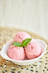 Strawberry ice cream with mint leaf. three balls in a white bowl on a vintage table. sorbet