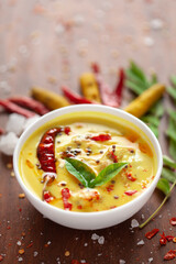 Close-up of Indian traditional kadhi or kadi pakora yogurt and gram flour and turmeric served hot in a clay bowl. garnished with fry red chili and curry leaf