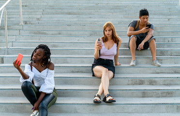 Fototapeta premium Friends checking mobile phones sitting on stairs