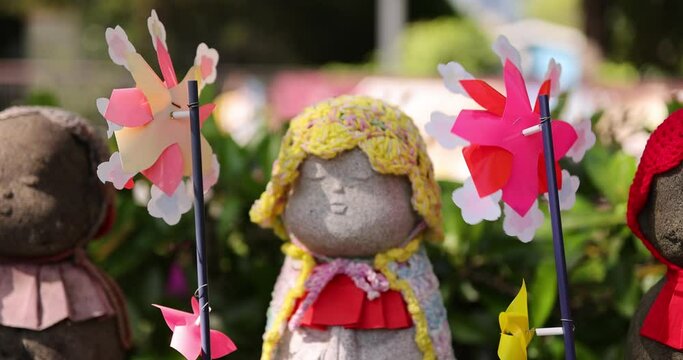 A slow motion of moving colorful windmills with Jizo statue daytime closeup