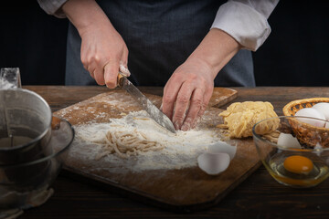 Women's hands, flour and dough. A woman in an apron cooking dough for homemade baking, a rustic home cozy atmosphere, a dark background with unusual lighting.