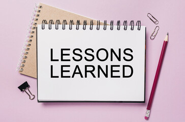 Text LESSONS LEARNED a white notepad with office stationery background. Flat lay on business, finance and development concept