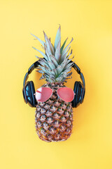 Pineapple hipster in sunglasses and headphones on yellow background. Summer concept. Top view, flat lay