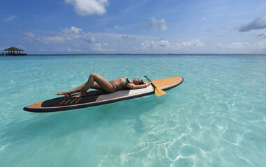 Fototapeta na wymiar girl in bikini lies on Surfboard in the ocean, Maldives