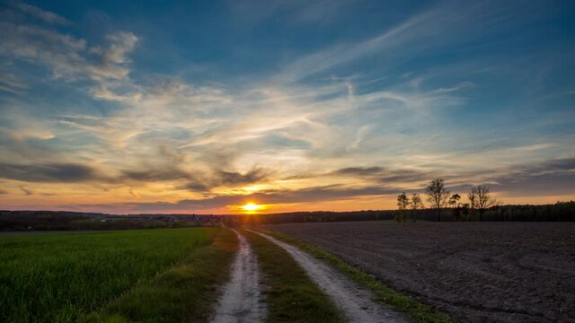 4k timelapse with beautiful, dramatic sunset sky over spring field and road