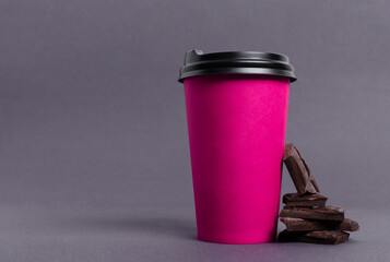 Closeup of pink paper cup of hot chocolate and pieces of dark chocolate on the grey surface.Empty space