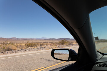 view in the rearview mirror of a car driving on a road in the middle of the desert under a blue sky