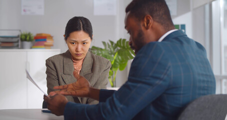 Angry african male boss shouting at young female employee pointing at report mistake