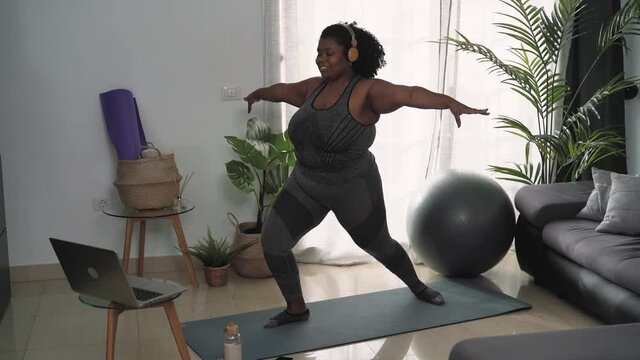 Young curvy African woman doing pilates virtual fitness class with laptop at home - Sport wellness people lifestyle concept